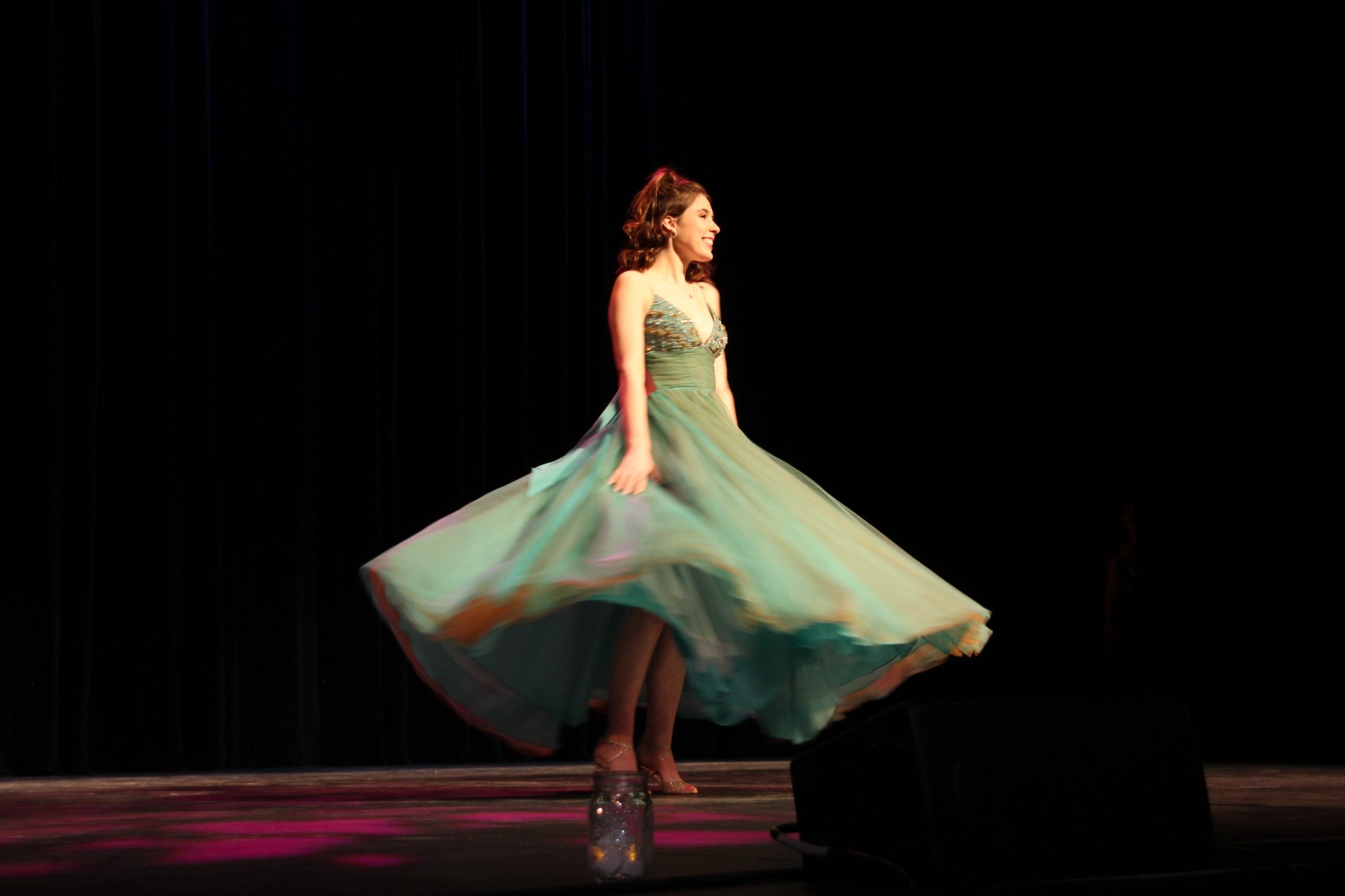 Woman twirls in a green gown onstage at Fashion for Freedom's annual fashion show.