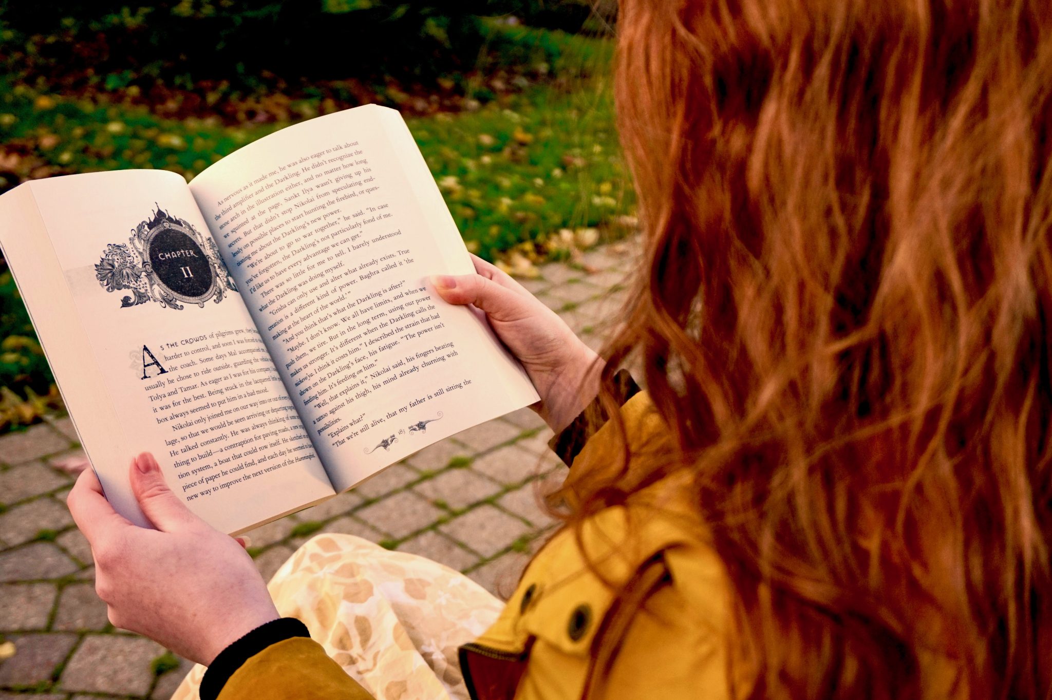 A girl with long red hair reading a novel.