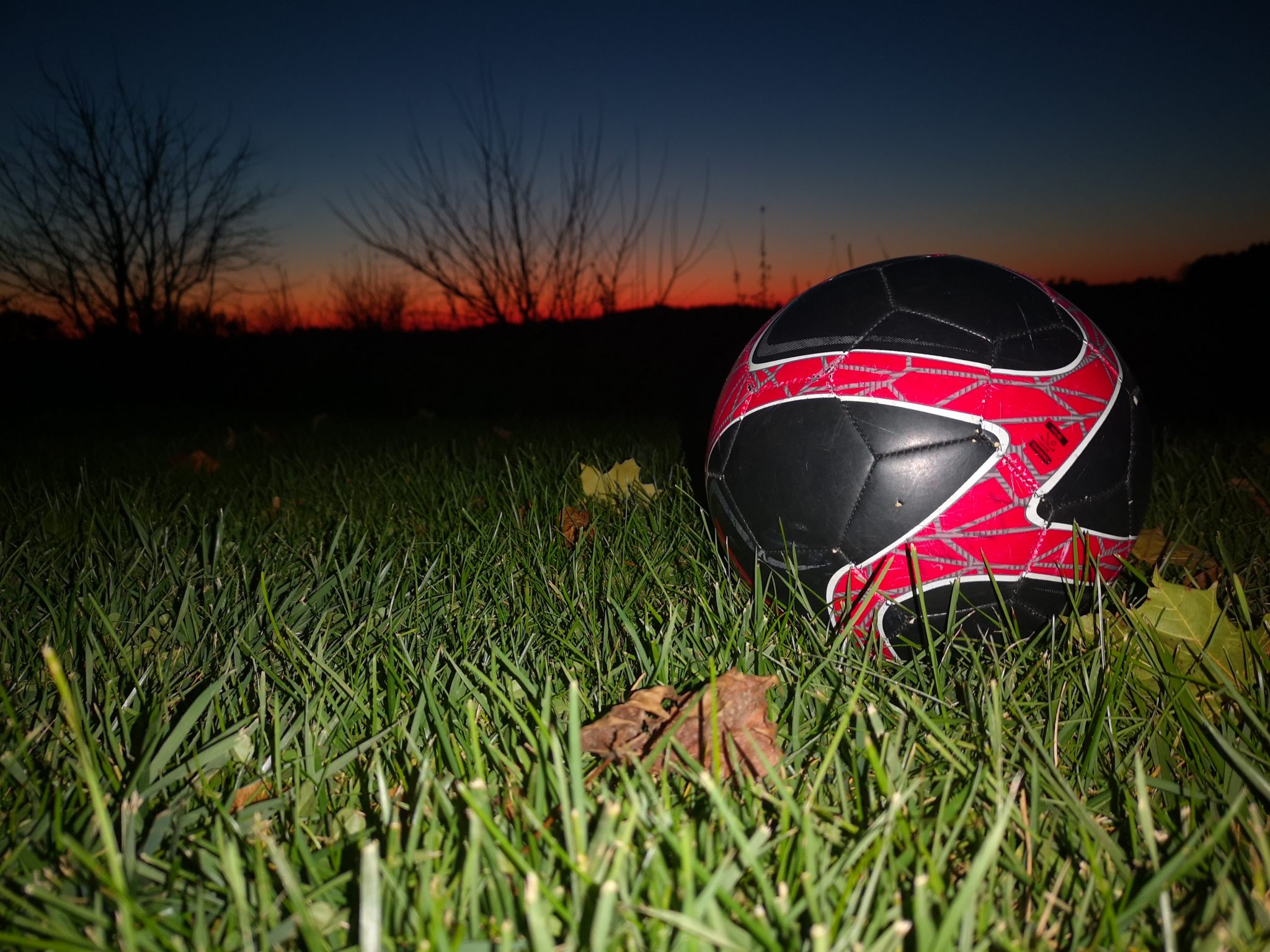 Black and red soccer ball in a field as the sun sets