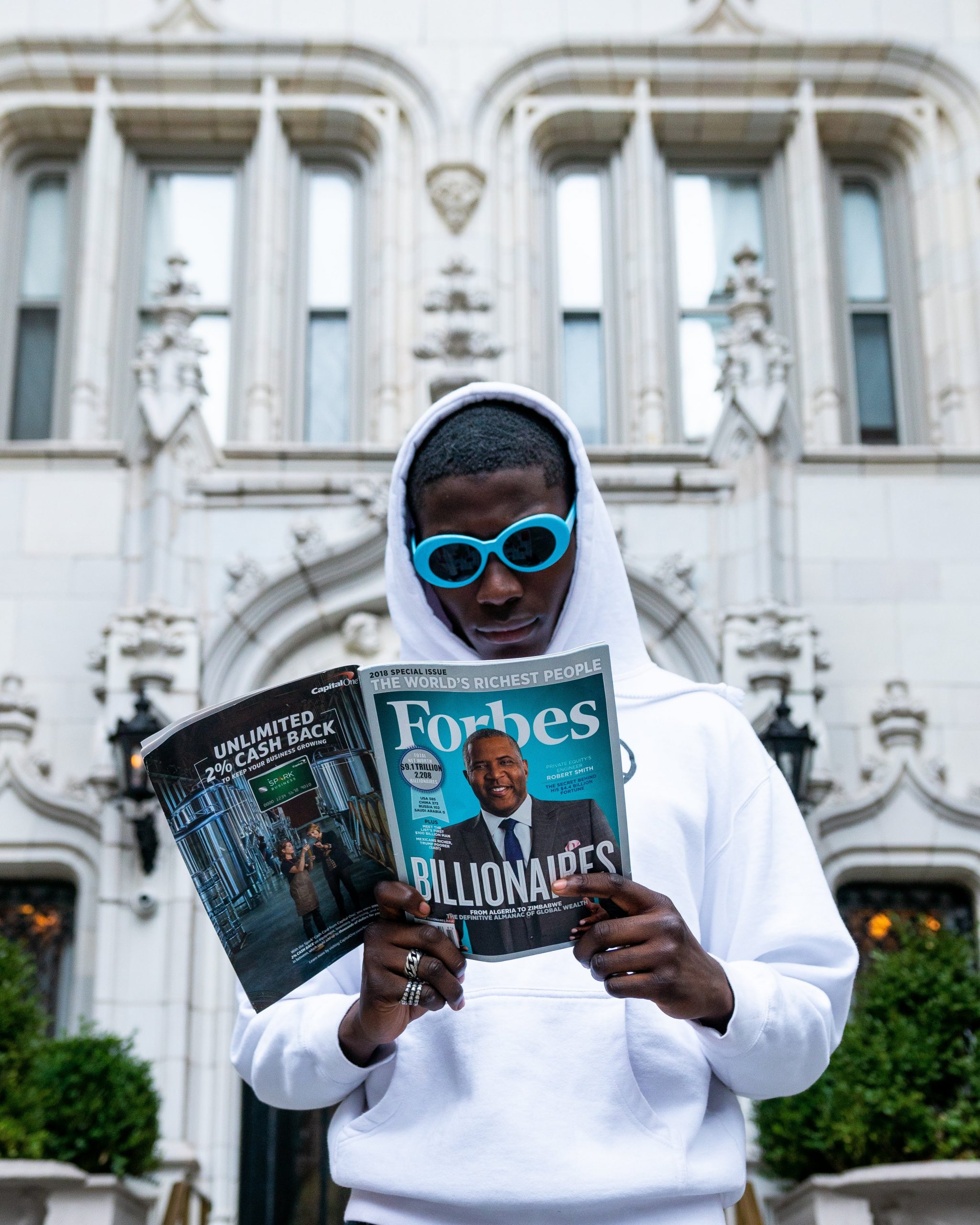A man reading Forbes magazine, "Billionare" is on the cover with a man in a suit.