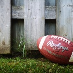 A football lying on grass with a wood fence in the background