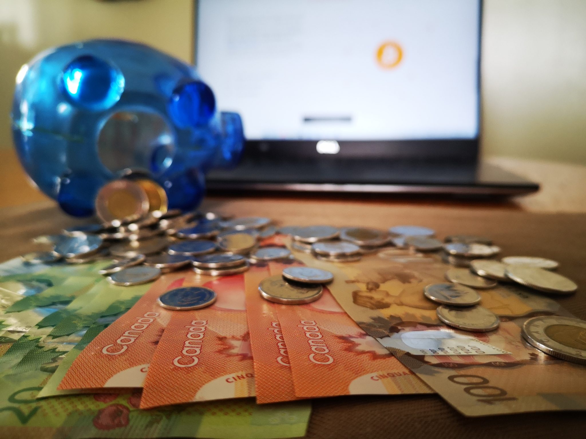 Money and a piggybank laid out infront of a laptop