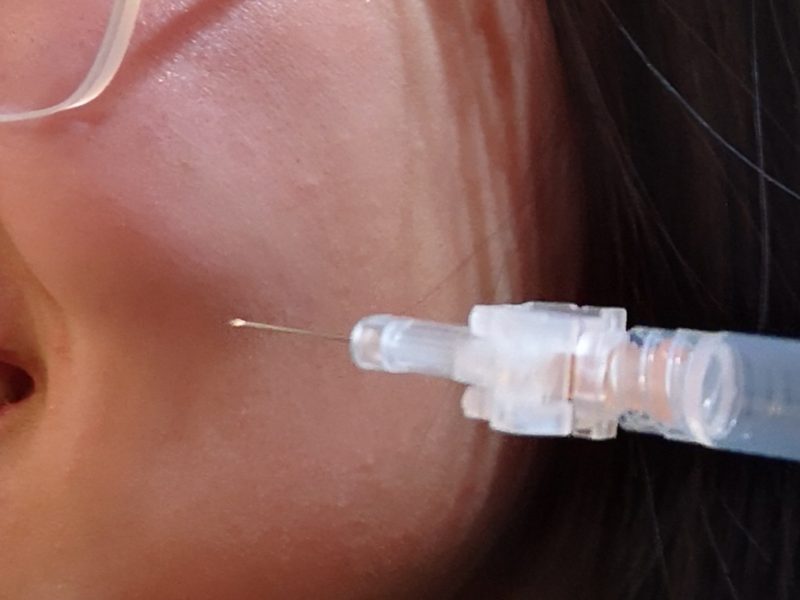 A syringe being held beside someone's cheek