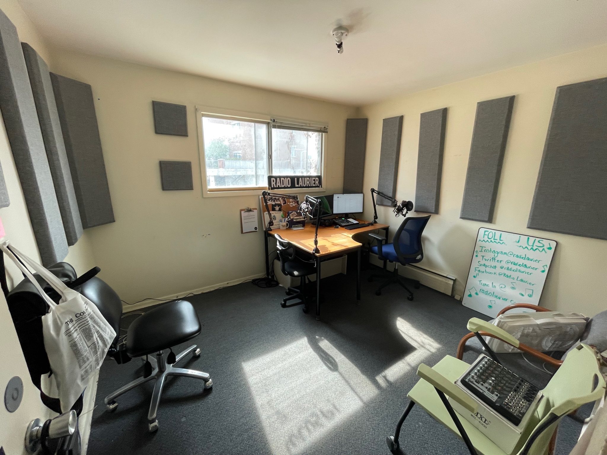 a large room with a chair in one corner and a desk with a computer diagonal from it. the walls also have medium grey rectangles to assisst with soundproofing and reducing echo