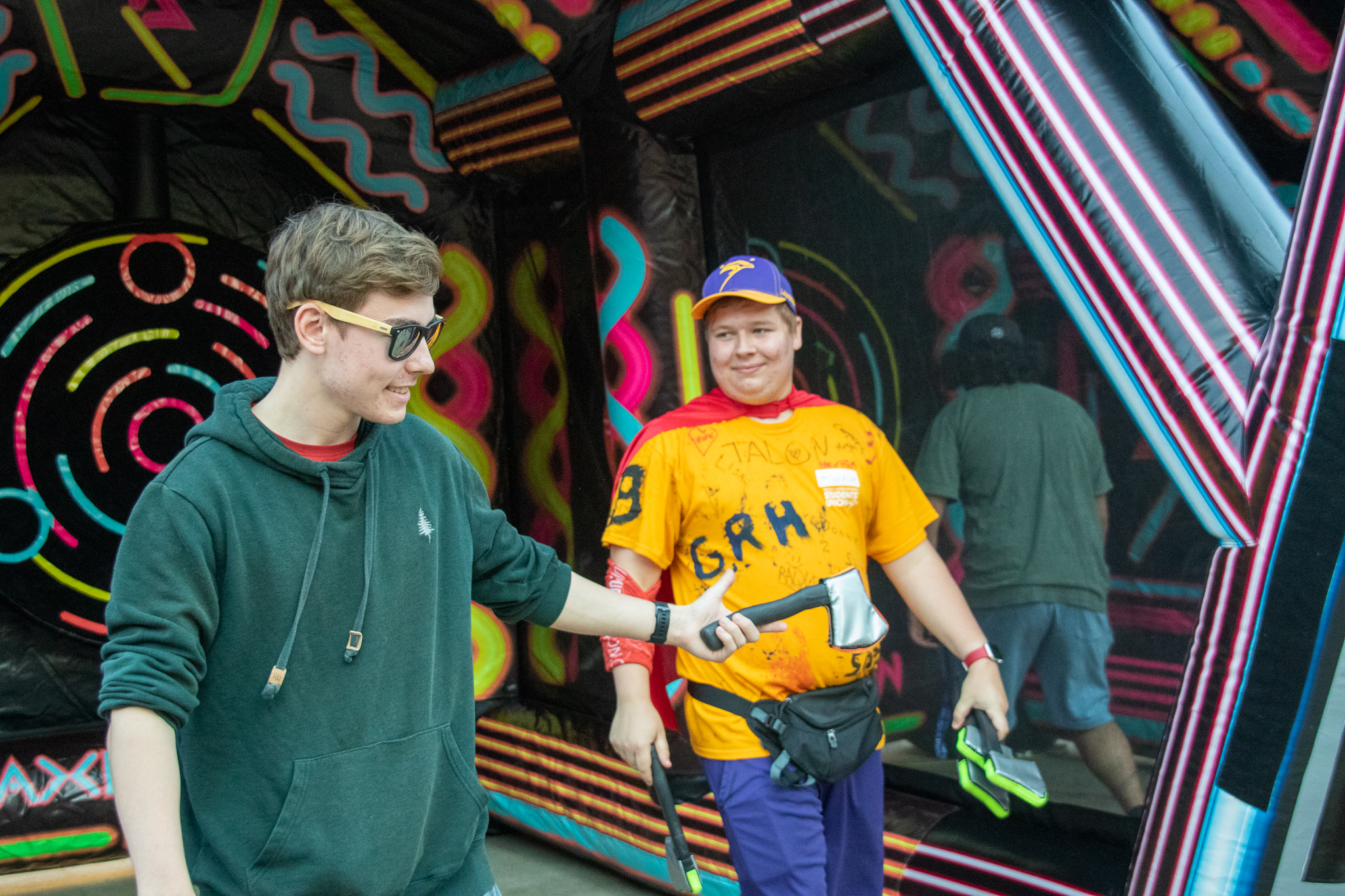 two students in front of a black wall with neon colours painted on it