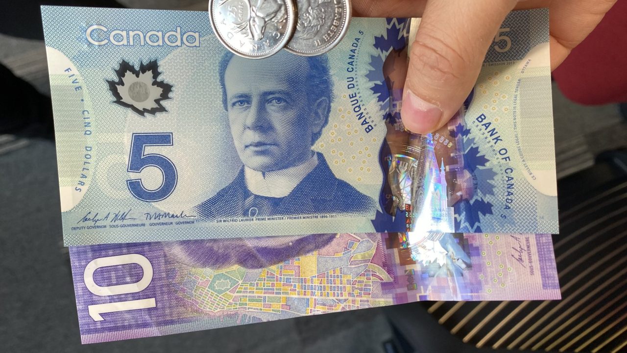 Canadian blue 5 and purple 10 dollar bills and 2 quarters in someone's hand