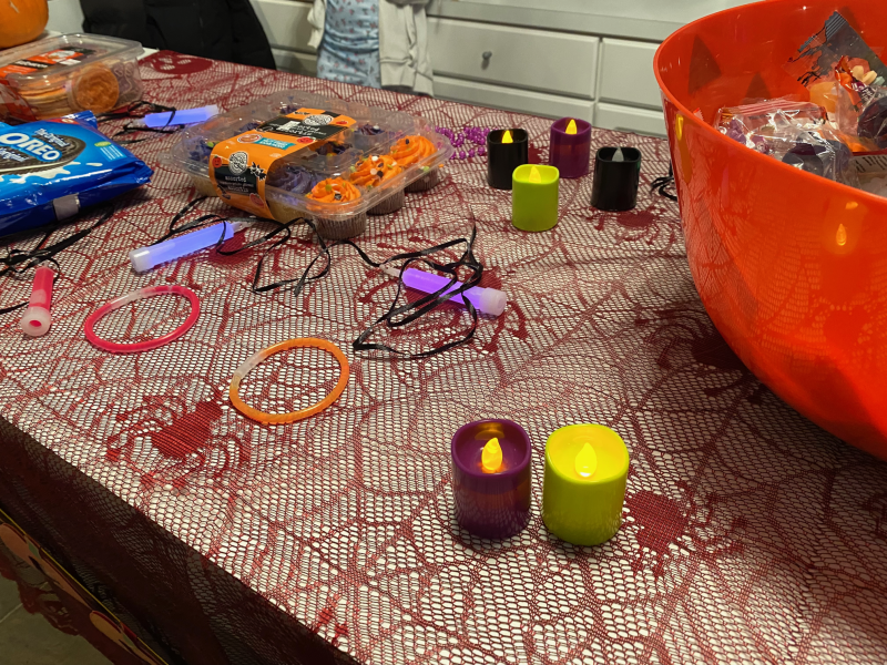 a bucket of halloween candy, on a table with a red table cloth. there are an assortment of halloween type items on the table