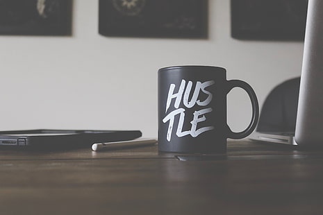 Black mug that reads hustle beside an ipad and apple pen